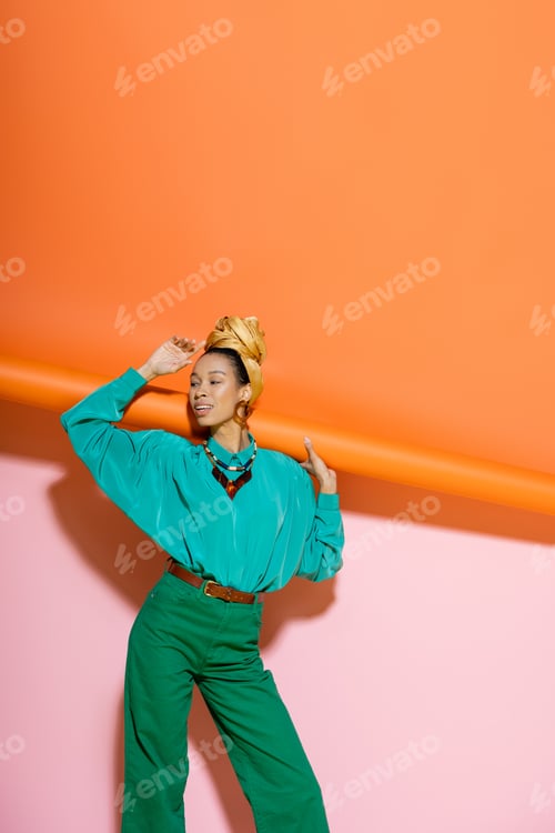 Preview: Trendy african american woman in bright summer outfit smiling on pink and orange background