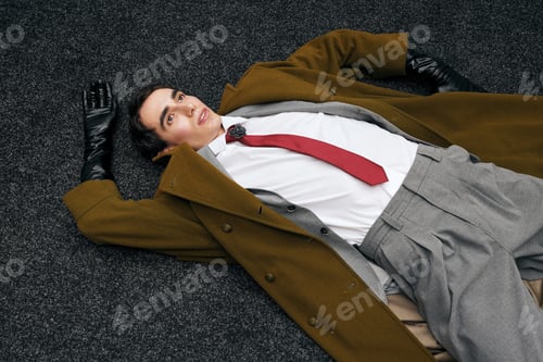 Preview: Stylish man in a fashionable outfit lies on textured flooring with a casual demeanor