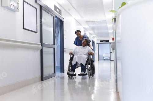 Preview: African american female doctor walking with senior female patient in wheelchair in hospital corridor