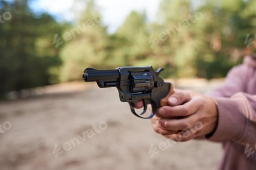 Preview: Female hand aiming revolver gun outdoors.