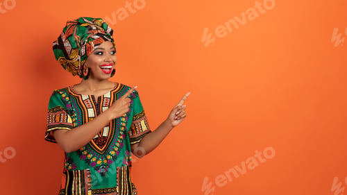 Preview: Excited beautiful black woman pointing at copy space on orange