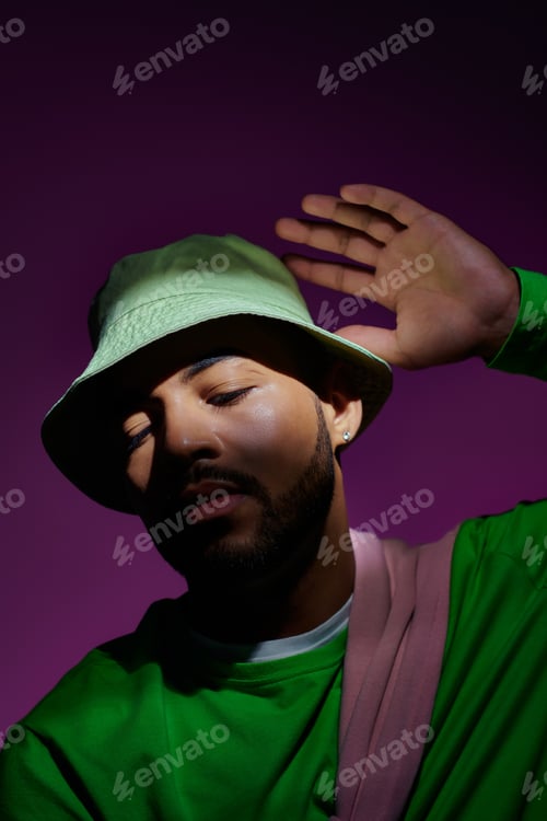 Preview: good looking man posing in green sweatshirt and panama with slightly raised hand, fashion concept