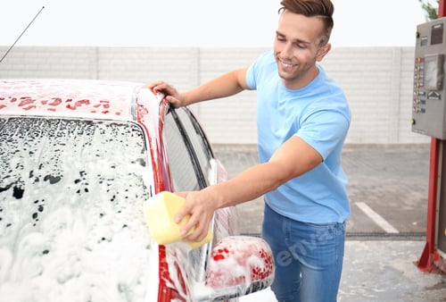 Preview: Young man cleaning vehicle with sponge at self-service car wash
