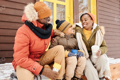 Preview: Cheerful black woman in winterwear looking at her cute son during talk