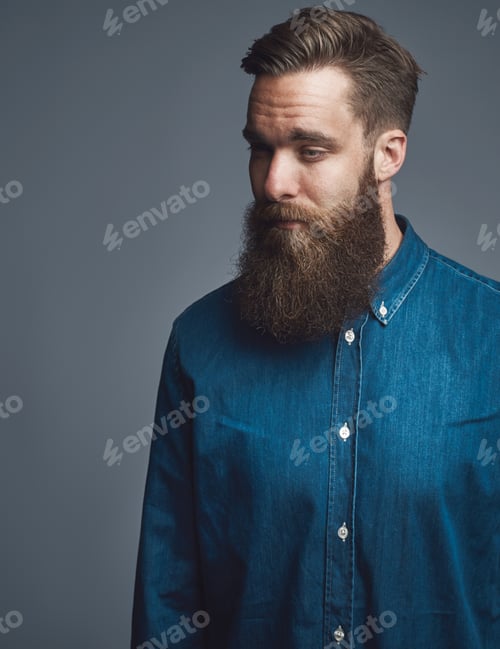 Preview: Bearded young man standing pensively against a gray background