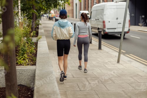 Preview: Two sportive young female friends walking city after morning running. Back view