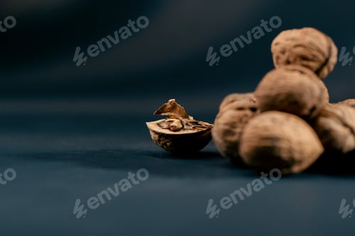 Preview: close-up on dark blue background with side lighting lie whole and split walnuts autumn fruits