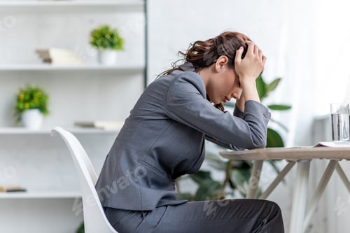 Preview: exhausted businesswoman holding hands near head while suffering from head in office