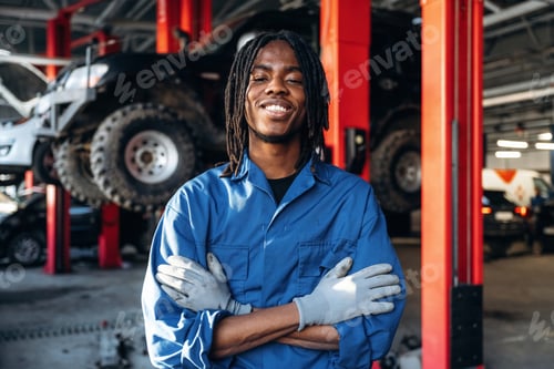 Preview: Dreadlocks hairstyle, in blue uniform. Male mechanic is with car in garage