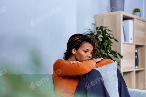 Preview: Depressed African woman feeling sad and tired, sitting alone in the living room.