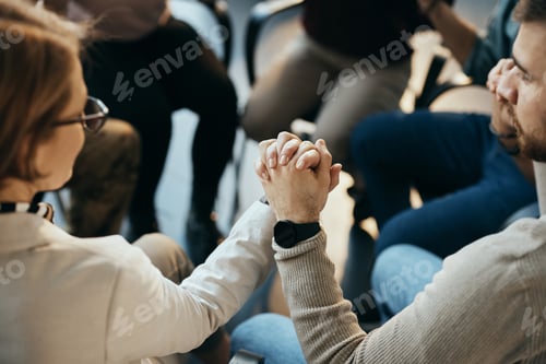 Preview: Close-up of participants of mental health group therapy holding hands while sitting in circle.