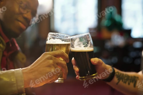 Vista previa: Hands of two young intercultural men clinking with glasses of beer in the pub