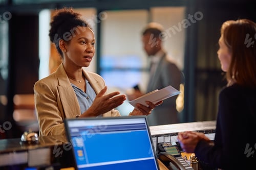 Preview: Black businesswoman talking to a receptionist while checking in at the hotel.