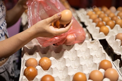 Preview: Close up of young woman hands selecting egg in supermarket.