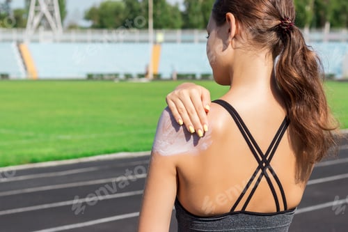 Preview: Young female runner standing and putting sun lotion on hand. Girl using sunscream before sport