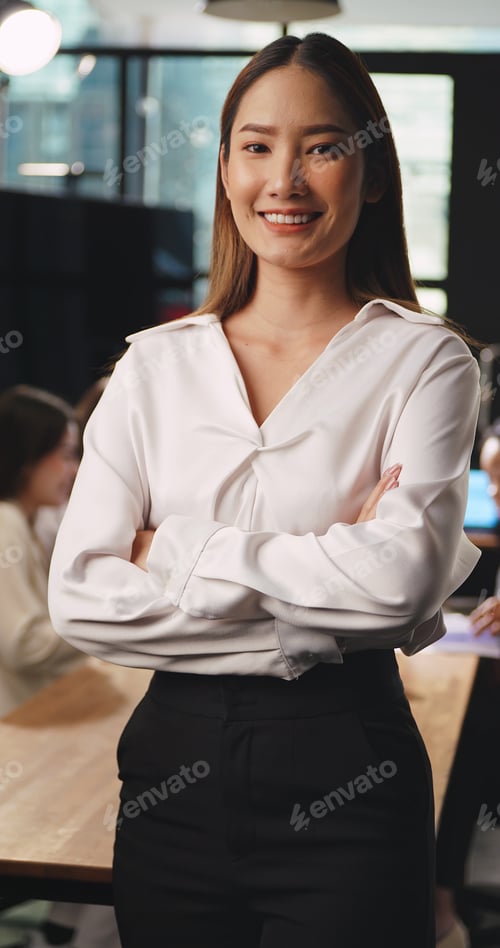 Preview: Portrait of young beautiful businesswoman standing with arms crossed looking at camera in office.