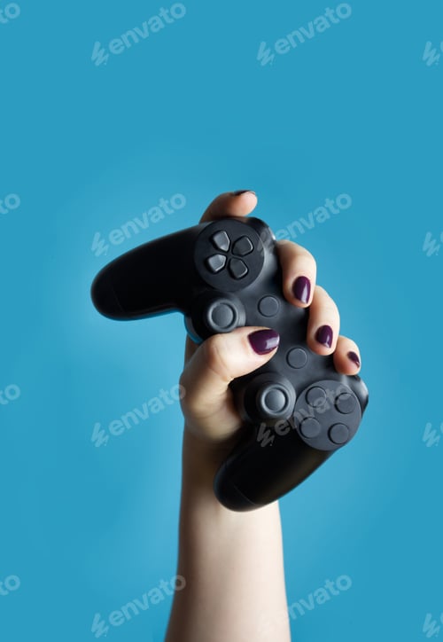 Preview: A female hand holds a controller from a video console on a blue background close-up