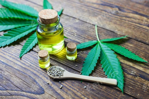 Preview: Hemp oil in glass jars wrapped in cannabis leaves, seeds on a wooden spoon nearby.