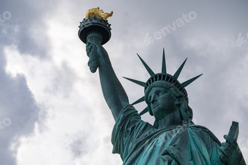 Preview: Majestic Statue of Liberty illuminated against a cloudy sky.