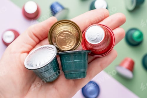 Preview: Female hand hold capsules for coffee machine on green and pink background, top view.