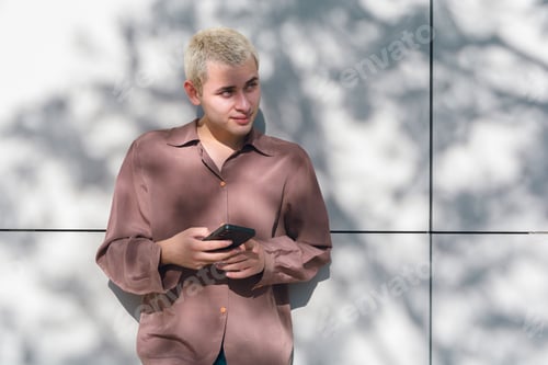 Preview: A young latin man with blonde hair is holding a cell phone outdoors