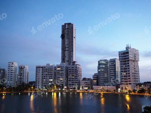 Preview: Cityscape of modern high-rise buildings reflected in a body of water at dusk with a clear blue sky