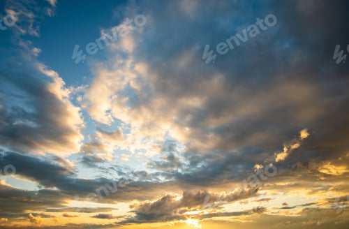 Vorschau: Dramatisch Sonnenuntergangslandschaft mit geschwollenen Wolken beleuchtet von orange untergehender Sonne und blauem Himmel