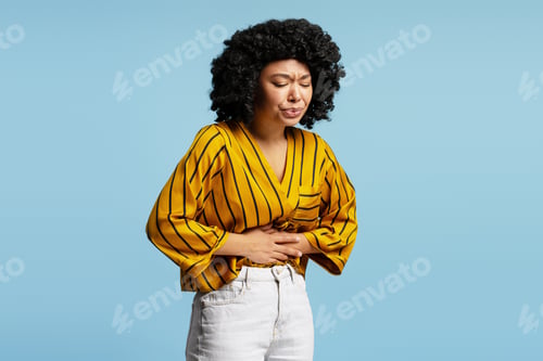 Preview: Young woman suffering from strong abdominal pain on blue background