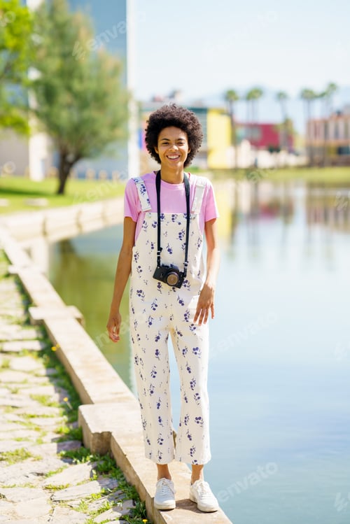 Preview: Content black woman with photo camera near lake