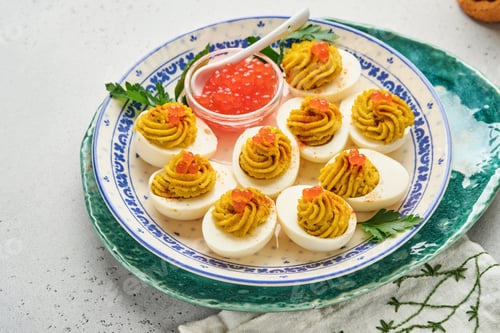 Preview: Stuffed eggs with red caviar and paprika on plate for appetizer easter table, top view, copy space.