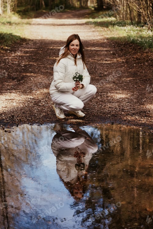 Preview: Woman Enjoying Nature, Holding Flowers Near a Tranquil Puddle in the Outdoors