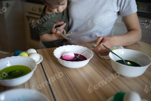 Preview: little cute boy paints eggs for easter sitting in the kitchen at the table