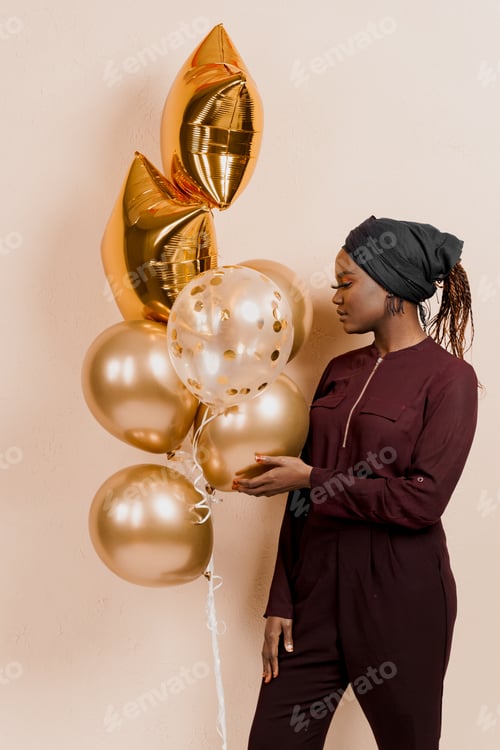 Preview: Muslim black girl with golden balloons on peach background. African woman birthday celebration