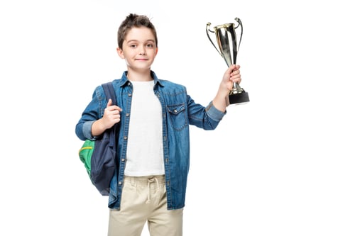 Preview: adorable schoolboy with backpack holding winner cup isolated on white