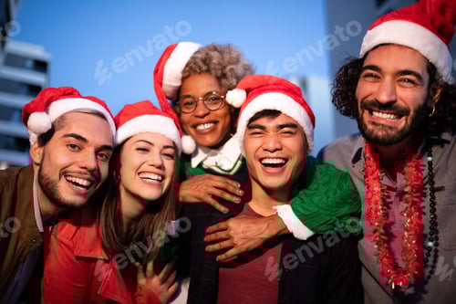 Visualização: Amigos multirraciais sorridentes usando chapéus de Papai Noel olhando para a câmera comemoram o Natal juntos.