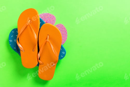 Preview: A lot of colored flip flops on green background. Top view with copy space