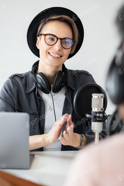 Vista previa: beautiful european woman with hat and glasses smiles and records podcast