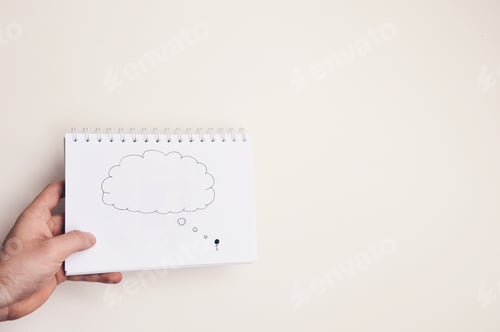 Preview: Hand holding a notebook with drawing of a person thinking on a white background