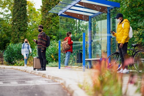 Preview: Young people with smartphones on bus stop outdoors in town. Coronavirus concept.