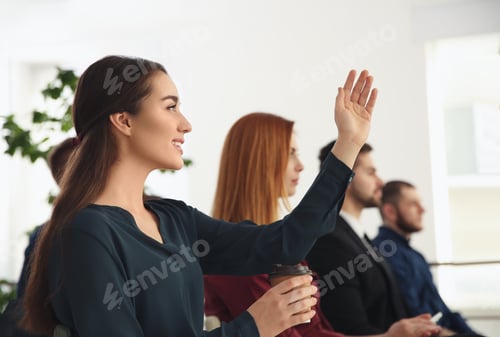 Preview: Young woman raising hand to ask question at business training indoors