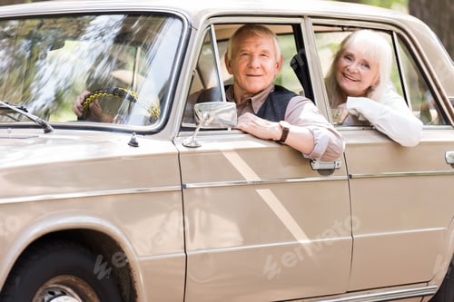 Preview: side view of attractive senior couple in beige car