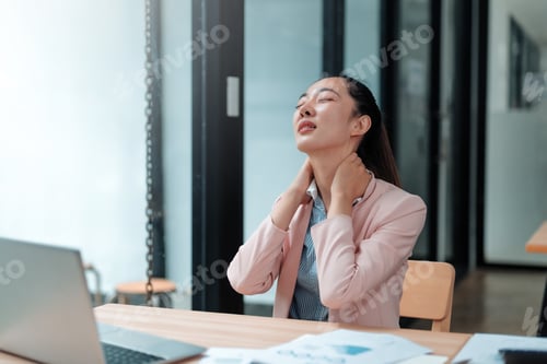 Preview: Asian businesswoman suffering from neck pain while working on laptop in office