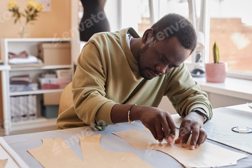 Preview: Young male owner of modern fashion studio contouring sewing paper patterns