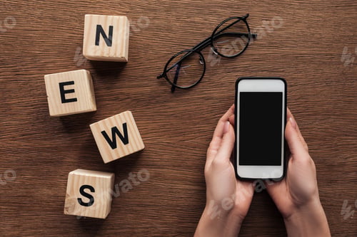Preview: cropped image of journalist holding smartphone, wooden cubes with word news on wooden table