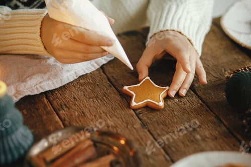 Preview: Hands decorating christmas gingerbread cookie star with icing on rustic table. Moody image