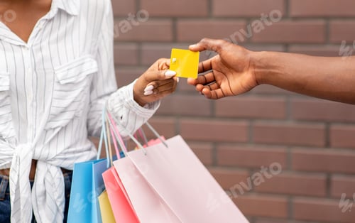 Preview: Female shopper with colored bags gives credit card to seller
