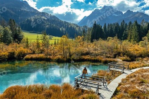 Vista previa: Woman sitting on wooden deck by idyllic lake surrounded by idyllic nature in autumn.