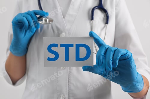 Preview: Doctor holding sheet of paper with abbreviation STD on white background, closeup