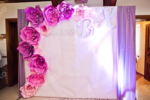 Preview: Wall deocrated with wedding couple's initials, big pink and purple flowers and curtains.