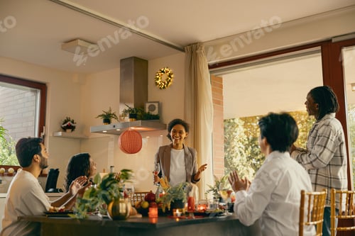 Preview: Group of smiling friends enjoying in conversation and drinking wine during Christmas party at home